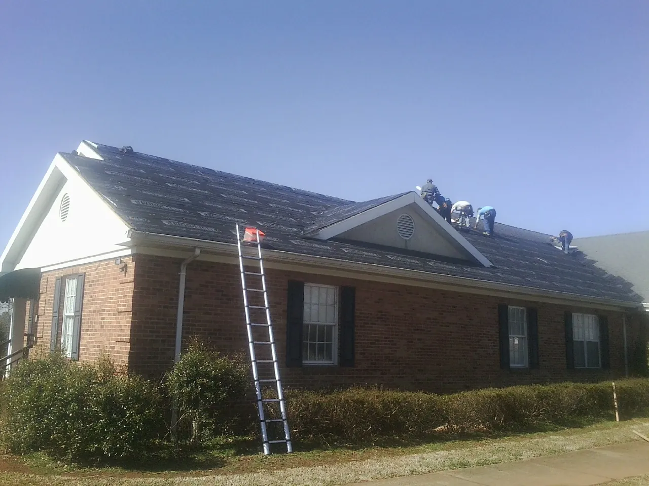Crew tearing shingles off a brick ranch roof with a ladder set — Emergency Roof Repair work by our crew in Clitherall