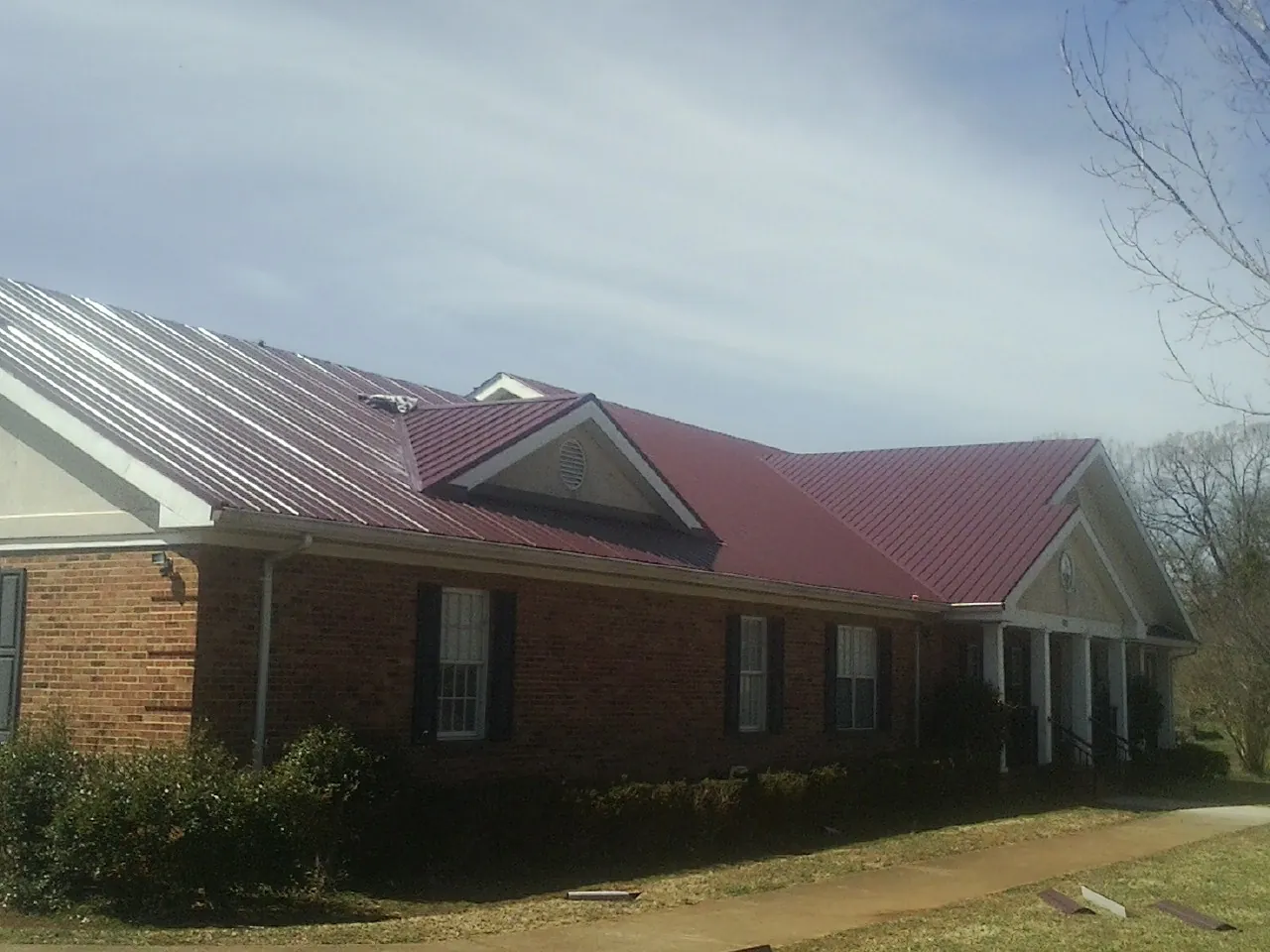 Red metal roof with gabled entries on a long brick building, from a Hail Damage Roof Repair job in Clitherall