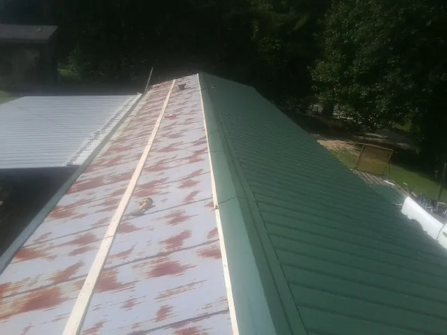 Old rusted panels beside newly installed green metal roofing — Wind Damage Roof Repair by Roofing Brothers in Clitherall