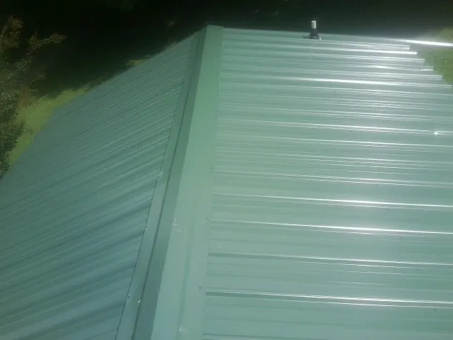 New green metal panels meeting at the ridge of a roof — Flat Roof Repair work by our crew in Clitherall