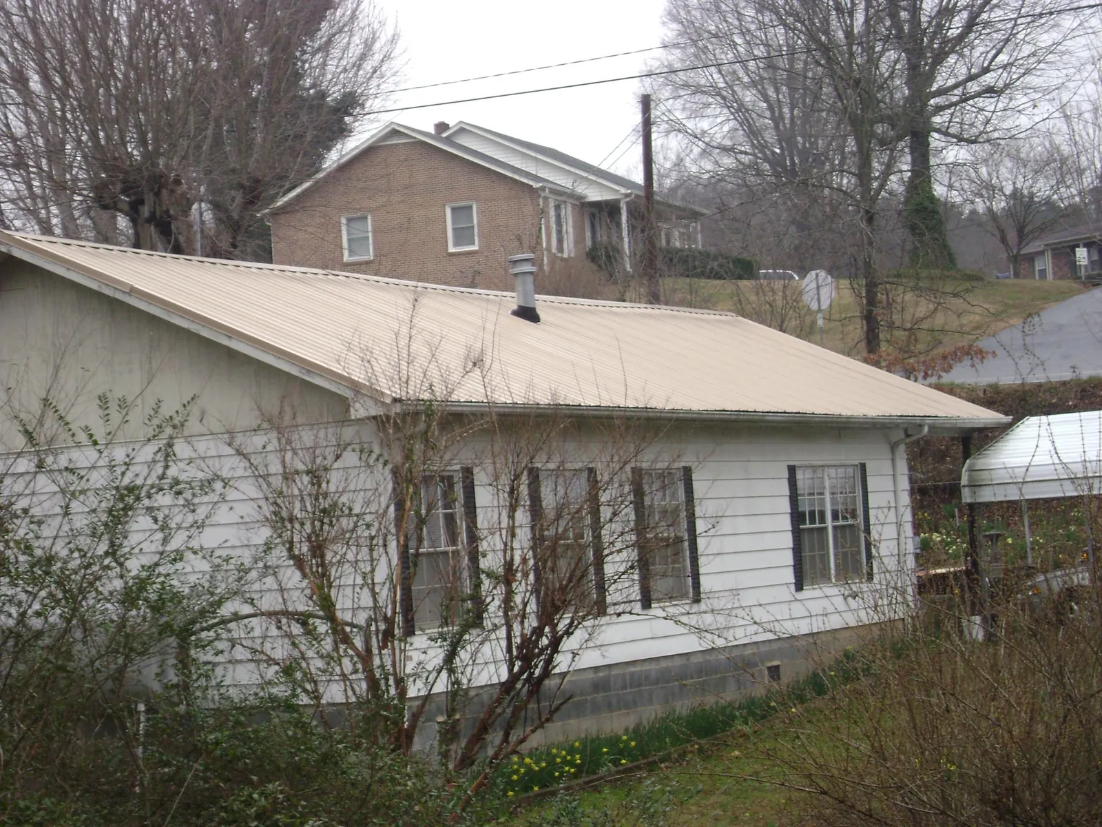 Tan metal roof on a white sided house set into a hillside — Commercial Roofing by Roofing Brothers in Clitherall