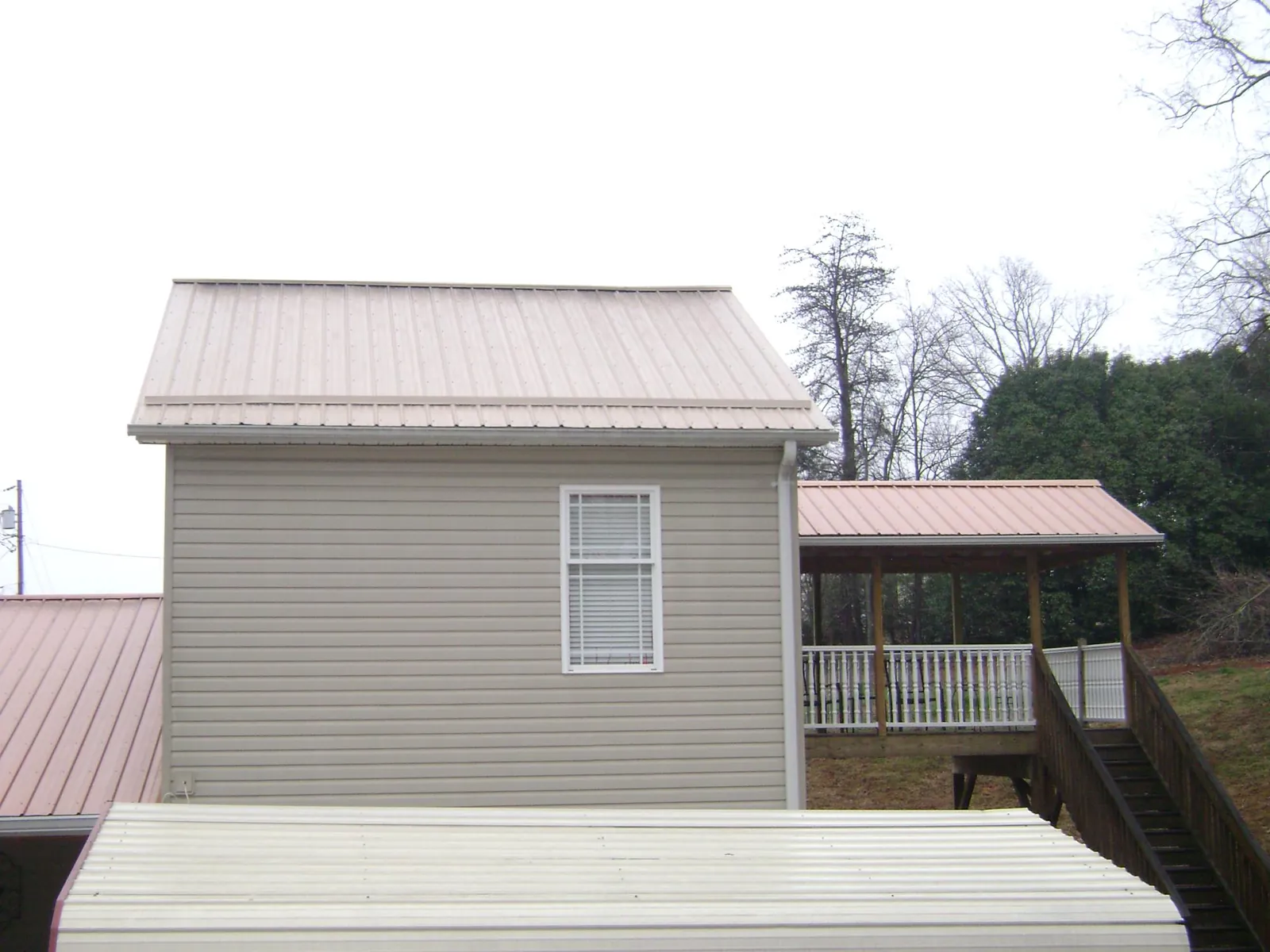 Tan metal roofs on a two story addition and attached porch, from a Roof Replacement job in Clitherall